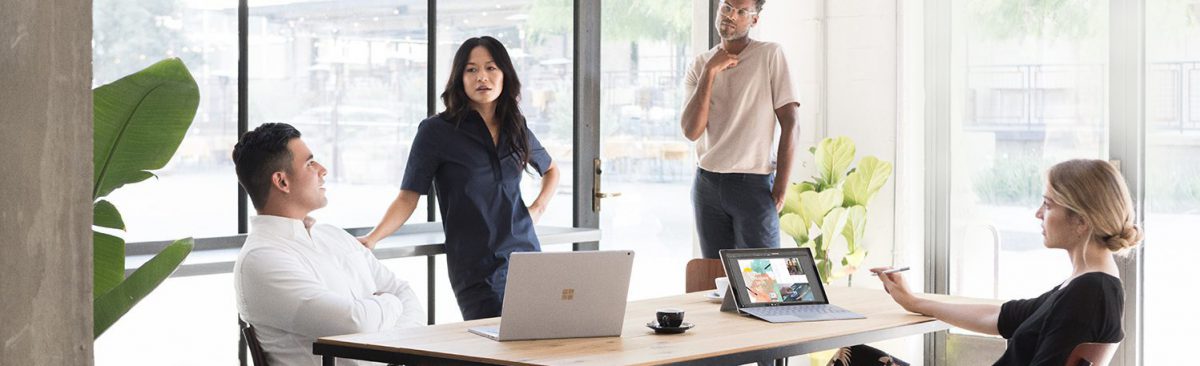 four people in a meeting with microsoft devices on a table