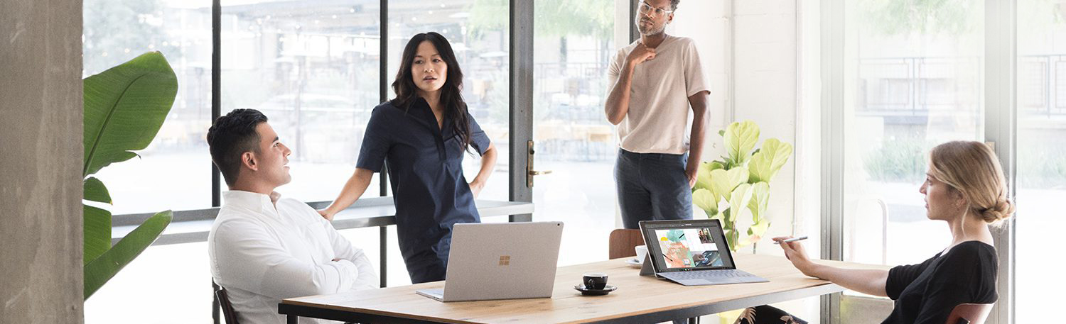 four people in a meeting with microsoft devices on a table