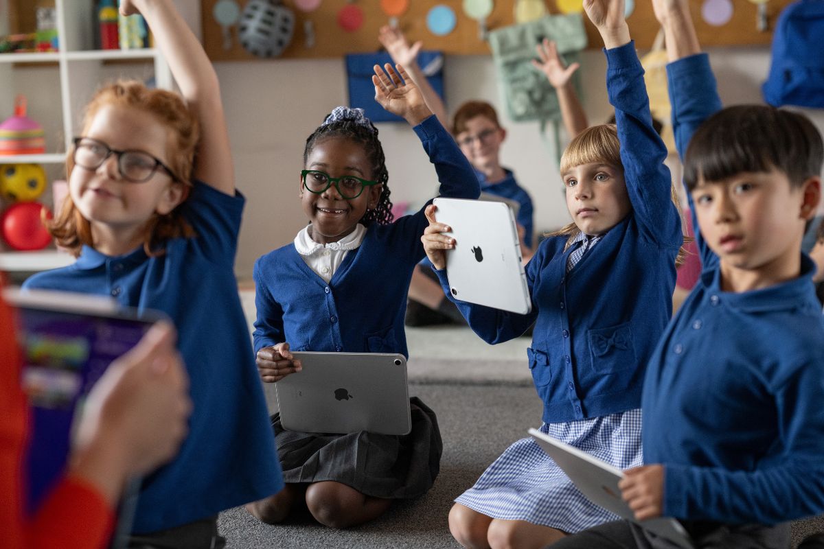 Children participating in lesson - raising hands with iPad in the other