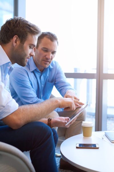Two,Businessmen,Sitting,In,A,Bright,Modern,Office,Space,,Using